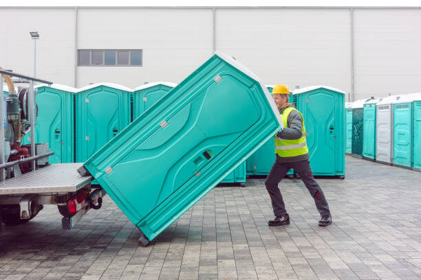 Crew member loading a teal portable restroom unit onto a delivery trailer